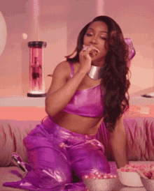 a woman in a purple outfit is sitting on a couch and eating candy