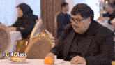 a man in a suit is sitting at a table with a plate of food .