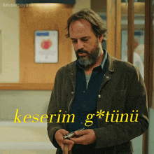 a man with a beard is holding a cell phone in front of a sign that says keserim