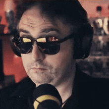 a man wearing sunglasses and headphones talks into a microphone