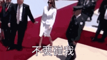 a woman in a white suit is walking on a red carpet with a man in a suit and tie .