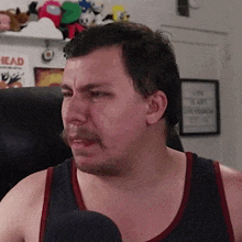 a man with a mustache is sitting in a chair in front of a microphone .