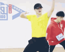 a man in a yellow shirt is dancing in front of a sign that says " 100 "