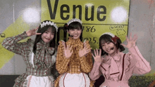 three girls dressed as maids are posing for a picture in front of a sign that says venue .