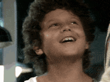 a young boy with curly hair is smiling and looking up at the sky