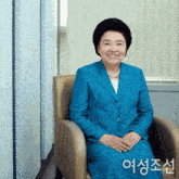 a woman in a blue suit sits in a chair and smiles