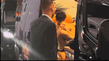 a man in a suit is standing next to a man in a wheelchair in front of a van that says ambulance on it