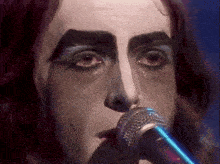 a close up of a person singing into a microphone with makeup on their face