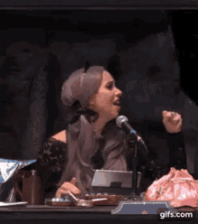 a woman is sitting in front of a microphone with the words `` no '' written on her face .