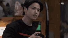 a young man is sitting at a table with a bottle of beer in his hand .