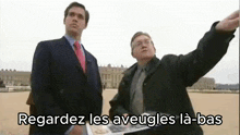 two men in suits and ties are standing next to each other and one of them is pointing .
