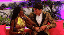 a man and a woman are sitting on a couch and the woman is wearing a gold dress