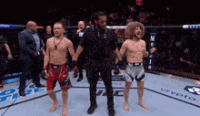 a referee stands between two men in a boxing ring .