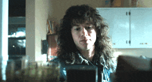 a man with long curly hair looks at something in a kitchen