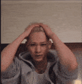 a man in a grey hoodie is holding his head with his hands
