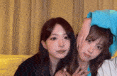two young women are sitting next to each other on a couch and looking at the camera .