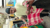 a man in a yellow shirt is holding a pink plaid cloth in front of a yellow and green vehicle