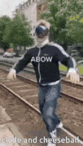 a man is standing on a train track wearing a jacket that says abow clyde and cheeseball .