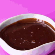 a white bowl of chocolate sauce on a pink surface