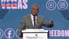 a man in a suit and tie stands at a podium in front of a sign that says freedom fest