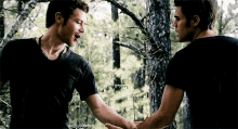 two men are shaking hands in the woods in front of trees .