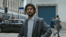 a man in a suit is walking down a street with a car in the background