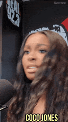 a woman says coco jones in front of a 92.3 sign
