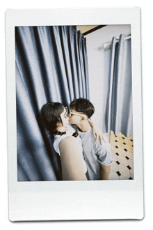 a man and woman kissing in front of a curtain
