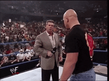a man in a suit is talking to a man in a black shirt in a wrestling ring