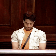 a man in an orange shirt sits at a table with his head down