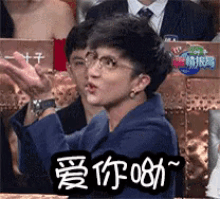 a man wearing glasses and a blue jacket is clapping his hands in a crowd .