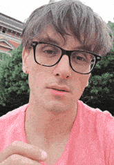 a man with glasses and a pink shirt looks at the camera