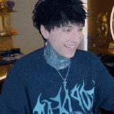 a young man with a tattoo on his neck is smiling while wearing a blue t-shirt and a necklace .