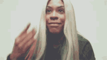 a woman with long blonde hair is making a funny face and waving her hand .