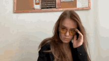 a woman wearing yellow sunglasses stands in front of a bulletin board