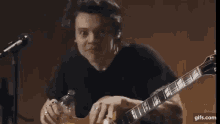 harry styles is playing a guitar in front of a microphone .
