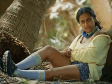 a woman wearing a yellow shirt and blue shorts is sitting under a tree