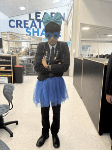 a person wearing a blue tutu and a bow stands in front of a wall that says learn create share