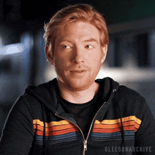 a man with red hair and a beard is wearing a black hoodie with a rainbow stripe