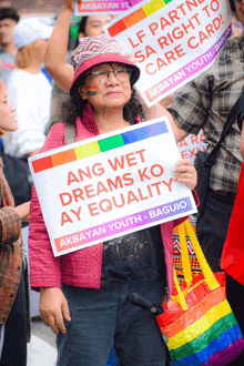 a woman in a pink jacket holds a sign that says ang wet dreams ko ay equality