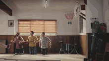 three men are dancing in a room with a basketball hoop hanging on the wall