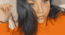 a close up of a woman 's face wearing an orange sweatshirt