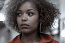 a woman with curly hair is wearing a red shirt and earrings and making a funny face .
