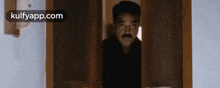 a man with a mustache is peeking out of a window .