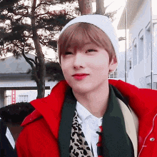 a young man wearing a red jacket and a white hat is looking at the camera .