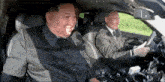 a man in a suit is driving a car with another man