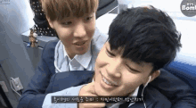 two young men are sitting next to each other and one of them is holding the other 's neck and smiling .