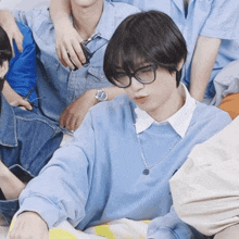 a man wearing glasses and a blue sweater is sitting in a group of people