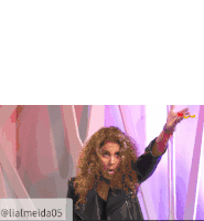 a woman with curly hair wearing a black leather jacket is standing in front of a purple background