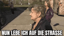 an elderly woman is standing on a sidewalk next to a little girl and says nun lebe ich auf die strasse .